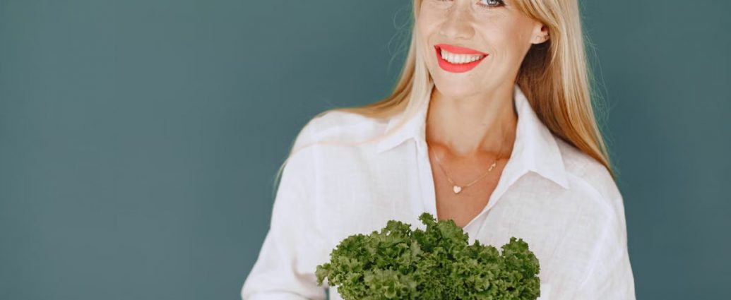 Cheerful woman with blonde hair holding fresh lettuce, promoting healthy living in a studio setting.