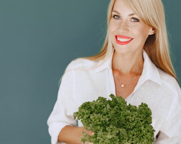 Cheerful woman with blonde hair holding fresh lettuce, promoting healthy living in a studio setting.