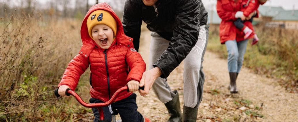 Father helping son ride a bicycle on a fall day while mother and daughter watch.