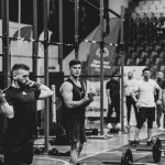 Black and white image of a fitness competition showcasing athletes and weights in a gym setting.