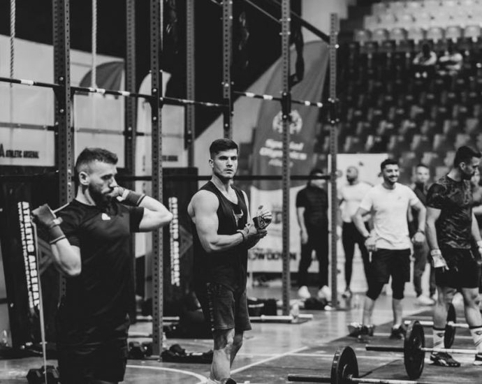 Black and white image of a fitness competition showcasing athletes and weights in a gym setting.